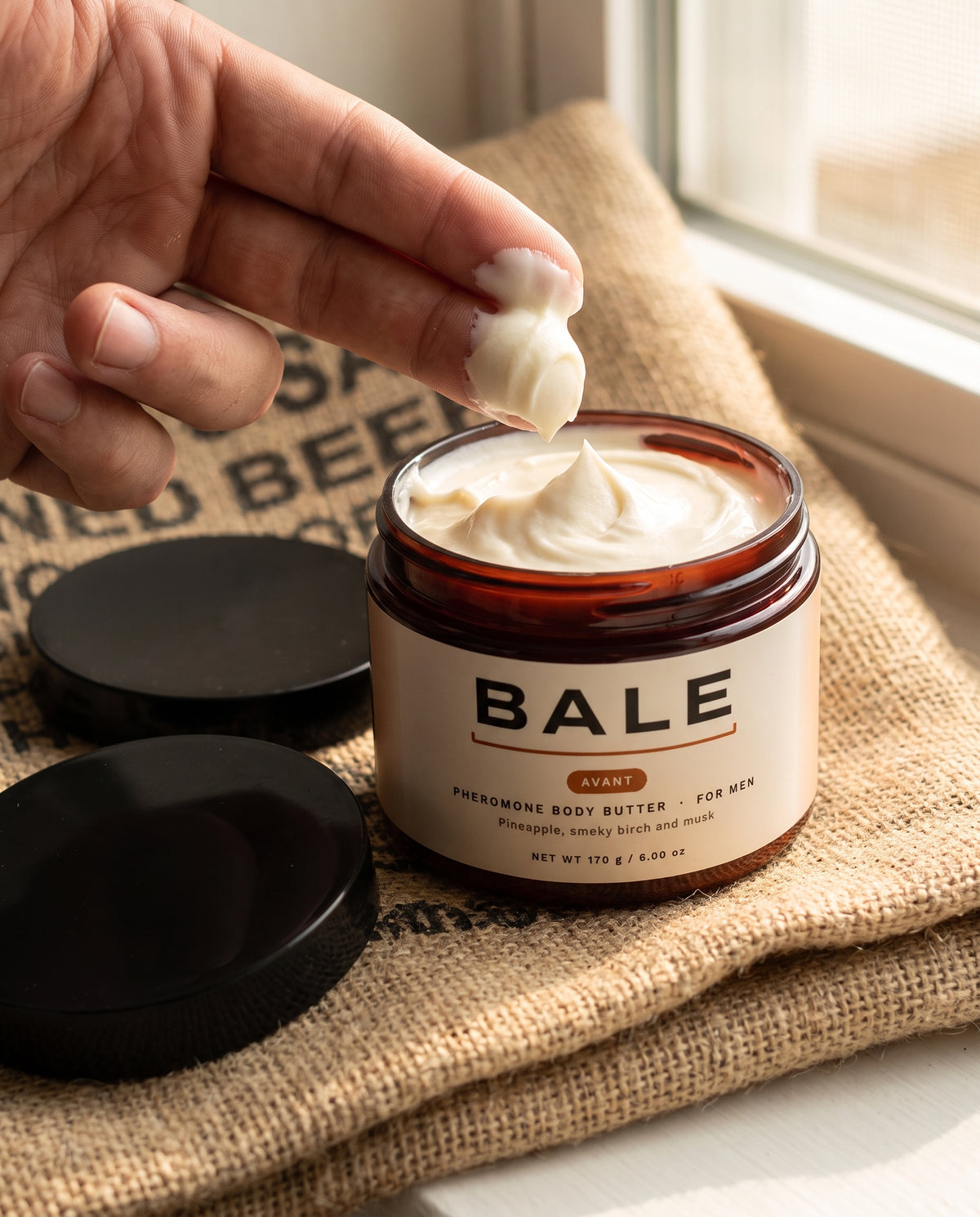 Finger taking a scoop of whipped Avant body butter on a coffee sack