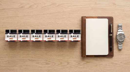 Six small Bale sample jars in a row on an oak desk beside a notebook, pen and watch