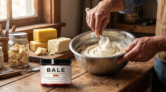 Hands folding whipped shea butter in a steel bowl in a workshop with a finished Bale jar in front