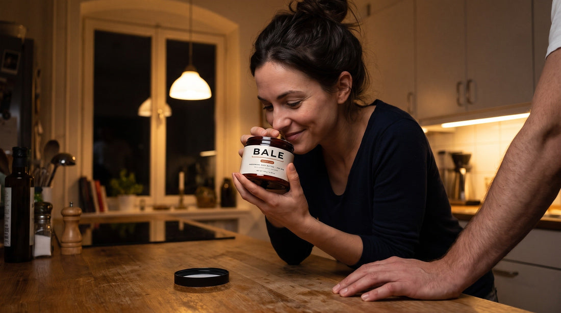 A woman smelling an open Bale jar in a warm kitchen while a man's hand rests on the counter