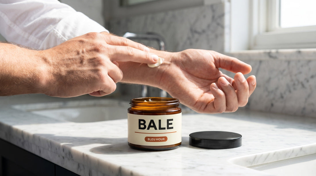 A man applying Bale Bleu Hour body butter to his wrist beside the open jar on a marble counter