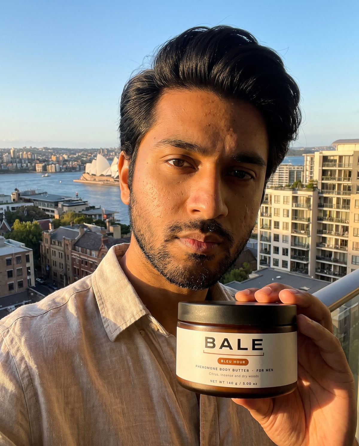 Man holding a jar of Bleu Hour body butter on a balcony at golden hour