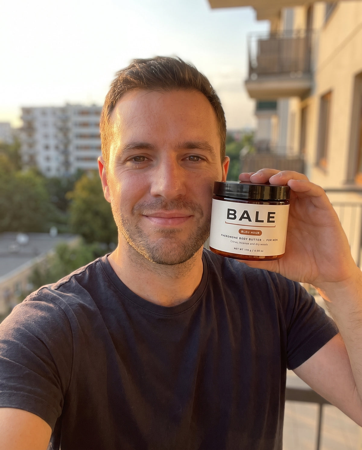 Man holding a jar of Bleu Hour body butter on a balcony at golden hour