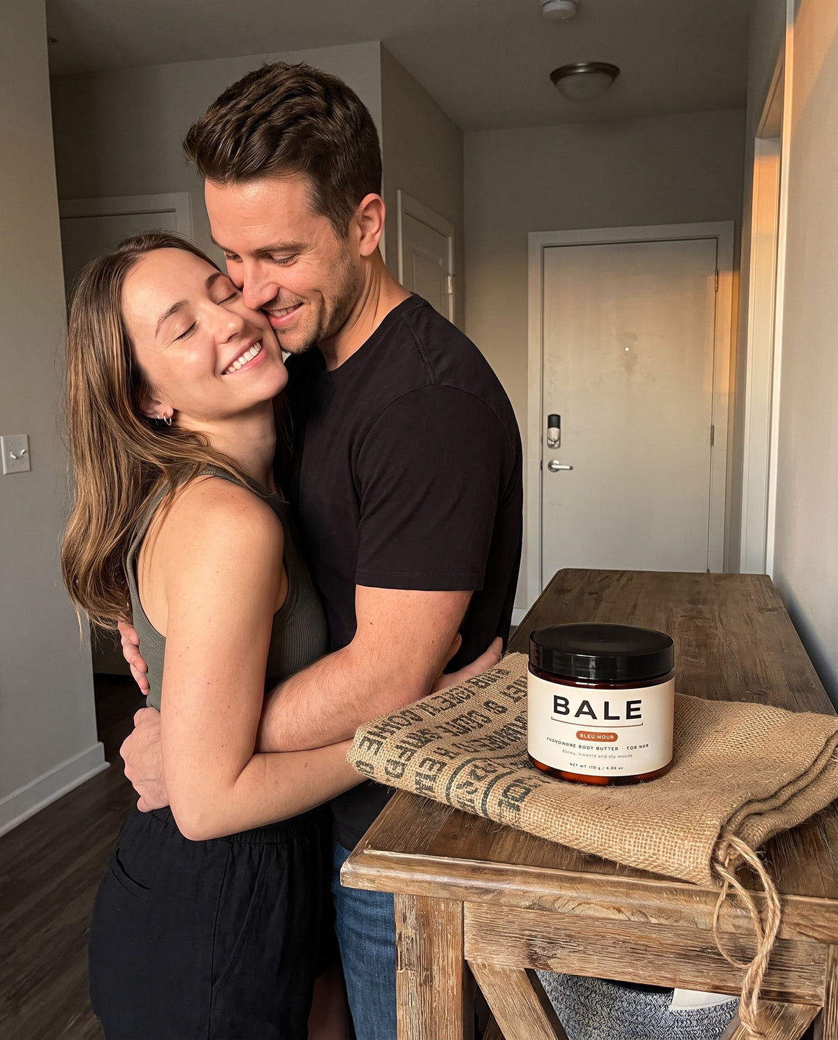 Couple hugging at the front door, Bleu Hour jar on a coffee sack wrap beside them