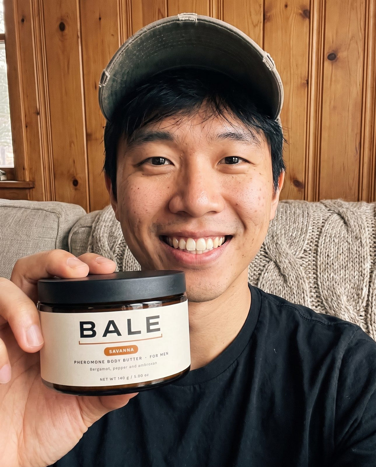 Man in a cap holding a jar of Savanna body butter, smiling