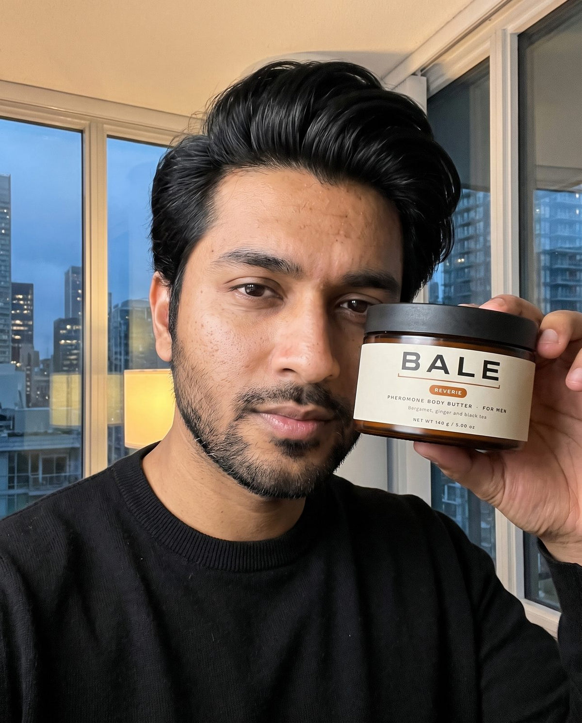 Man holding a jar of Reverie body butter while getting ready in the evening