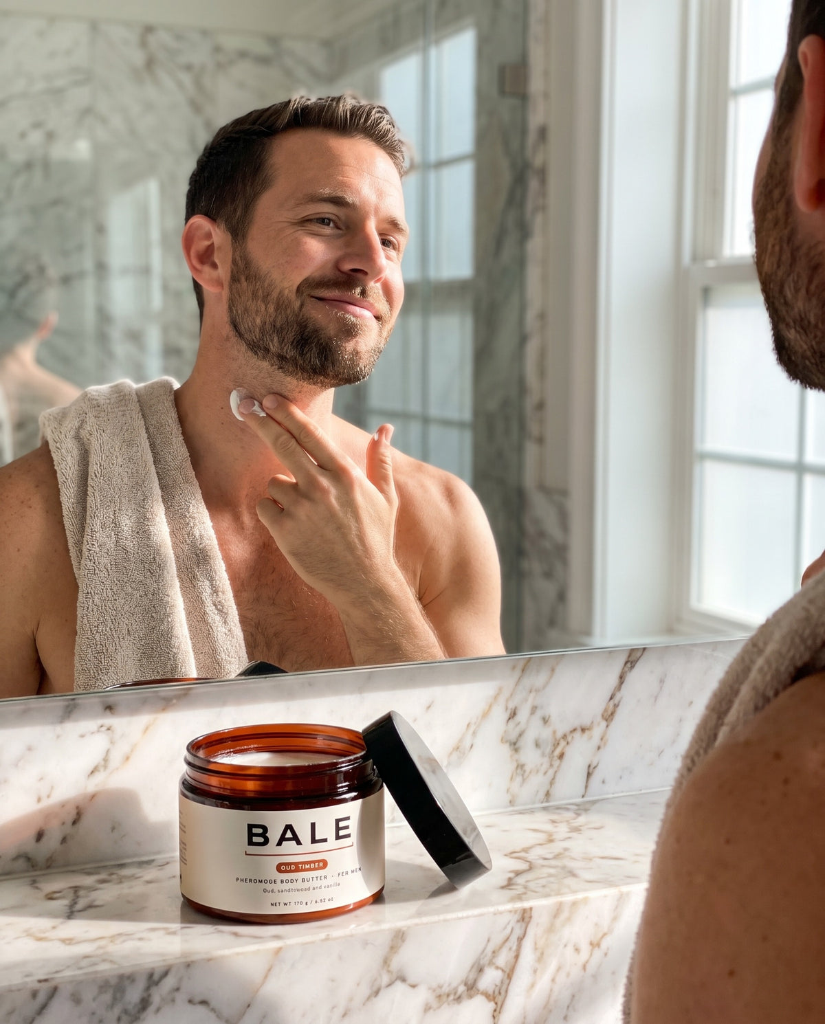Man pressing Oud Timber body butter into his neck before dinner, open jar on the counter