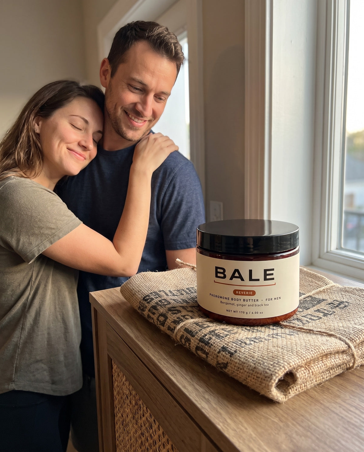 Couple hugging at the front door, Reverie jar on a coffee sack wrap beside them