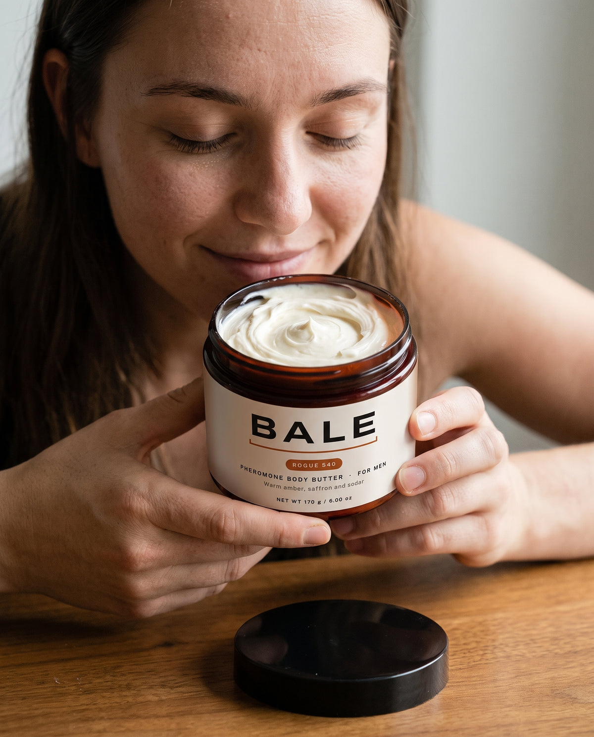 Woman smelling an open jar of Rogue 540 body butter with her eyes closed
