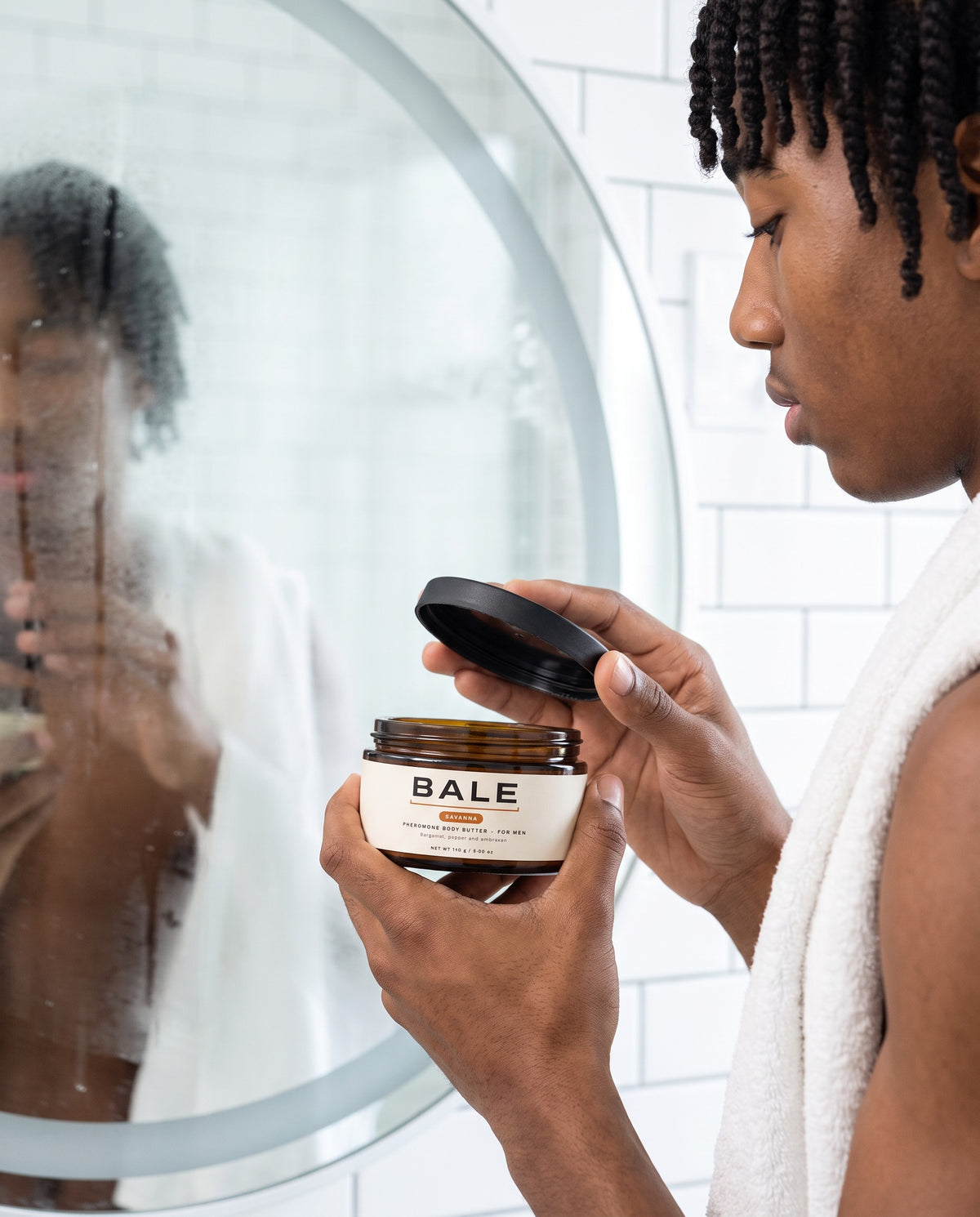 A man after a shower opening a jar of Bale Savanna body butter by the mirror
